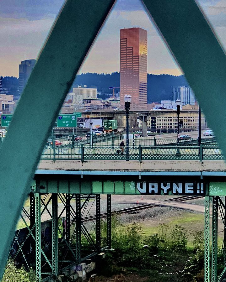 Green steel bridge truss framing a downtown Portland skyline